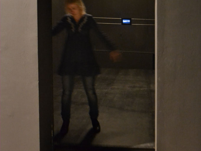 Kobieta wychodząca z pomieszczenia z instalacją wizualna w postaci małego ekranu.