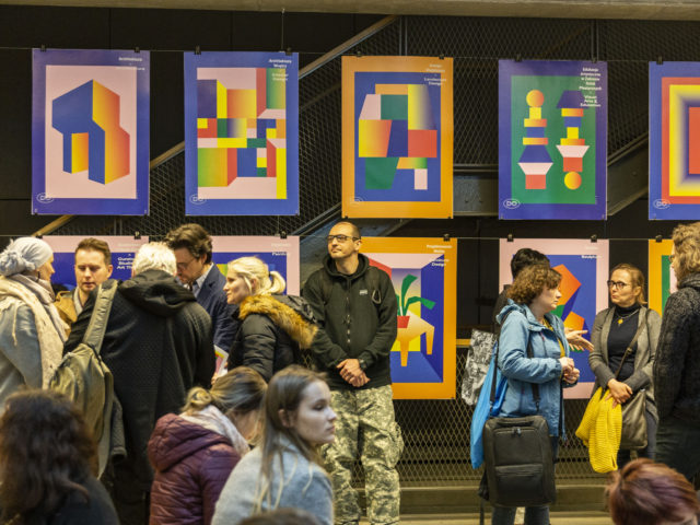 Ludzie zgromadzeni w sali Atrium w budynku B Uniwersytetu Artystycznego w Poznaniu podczas Drzwi Otwartych pomiędzy stoiskami poszczególnych kierunków i wydziałów.