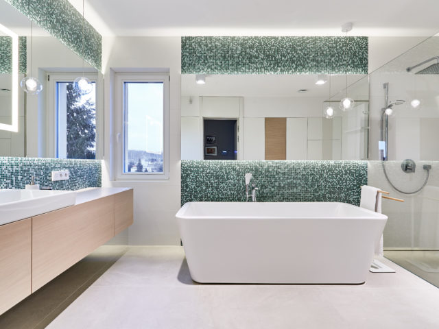 Łazienka; umywalka z dużym lustrem, odkryta wanna oraz przeszklony prysznic.