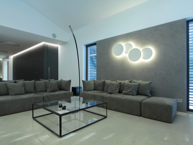 Salon; dwie duże kanapy, stolik kawowy, lapa stojąca, lampy w kształcie kół na ścianie.