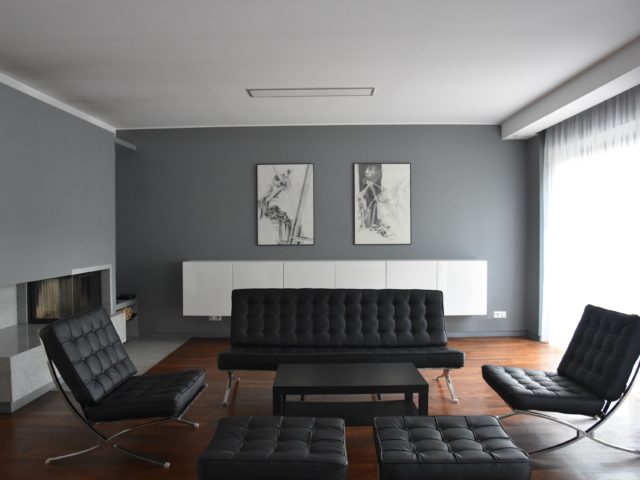 Projekt wnętrza domu jednorodzinnego, salon; kanapa, dwa fotele i pufy. Obrazy na ścianie. Kominek.