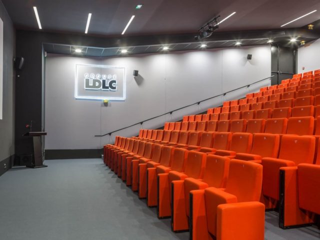 Sala wykładowa zaprojektowana dla firmy LDLC; rząd foteli kinowych, mównica do przemawiania, ekran do wyświetlania dla rzutnika. 