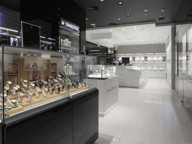 Wnętrze sklepu jubilerskiego "Swarovski". Oszklona wystawa zegarków, tle witryna z biżuterią.