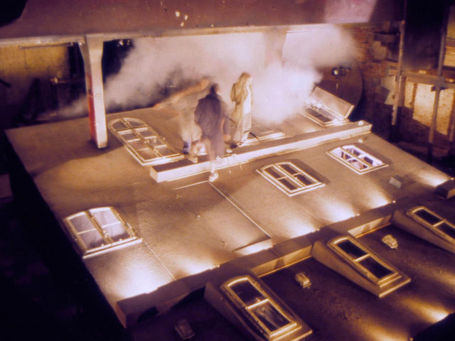 Aktorzy stojący na makiecie stylizowanej na fasadę budynku.