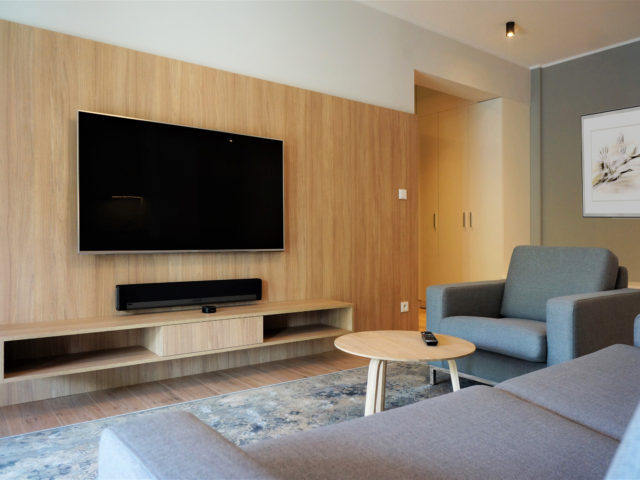 Salon; telewizor na ścianie, stolik kawowy, fotel i kanapa.