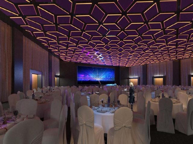 Sala konferencyjno- kongresowa; zastawione i przystrojone stoliki i krzesła, duży ekran na ścianie, kelnerka między stolikami.