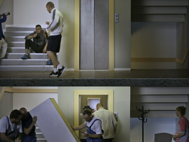 Klatka schodowa; na schodach trzech mężczyzn pijących alkohol i palących papierosy. Piętro niżej mężczyźni ładujący szafę do windy.