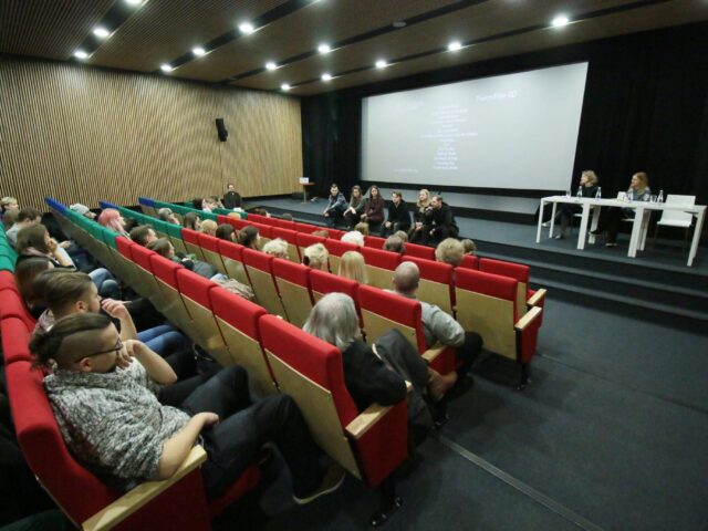 Spotkanie z autorami wystawy na panelu dyskusyjnym. Ludzie siedzący w fotelach sali wykładowej.