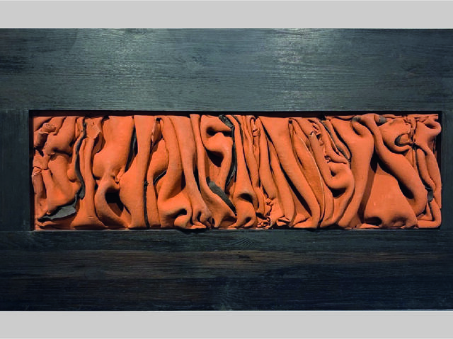 Pomarańczowy zgnieciony materiał wciśnięty w ramę z czarnych drewnianych desek.