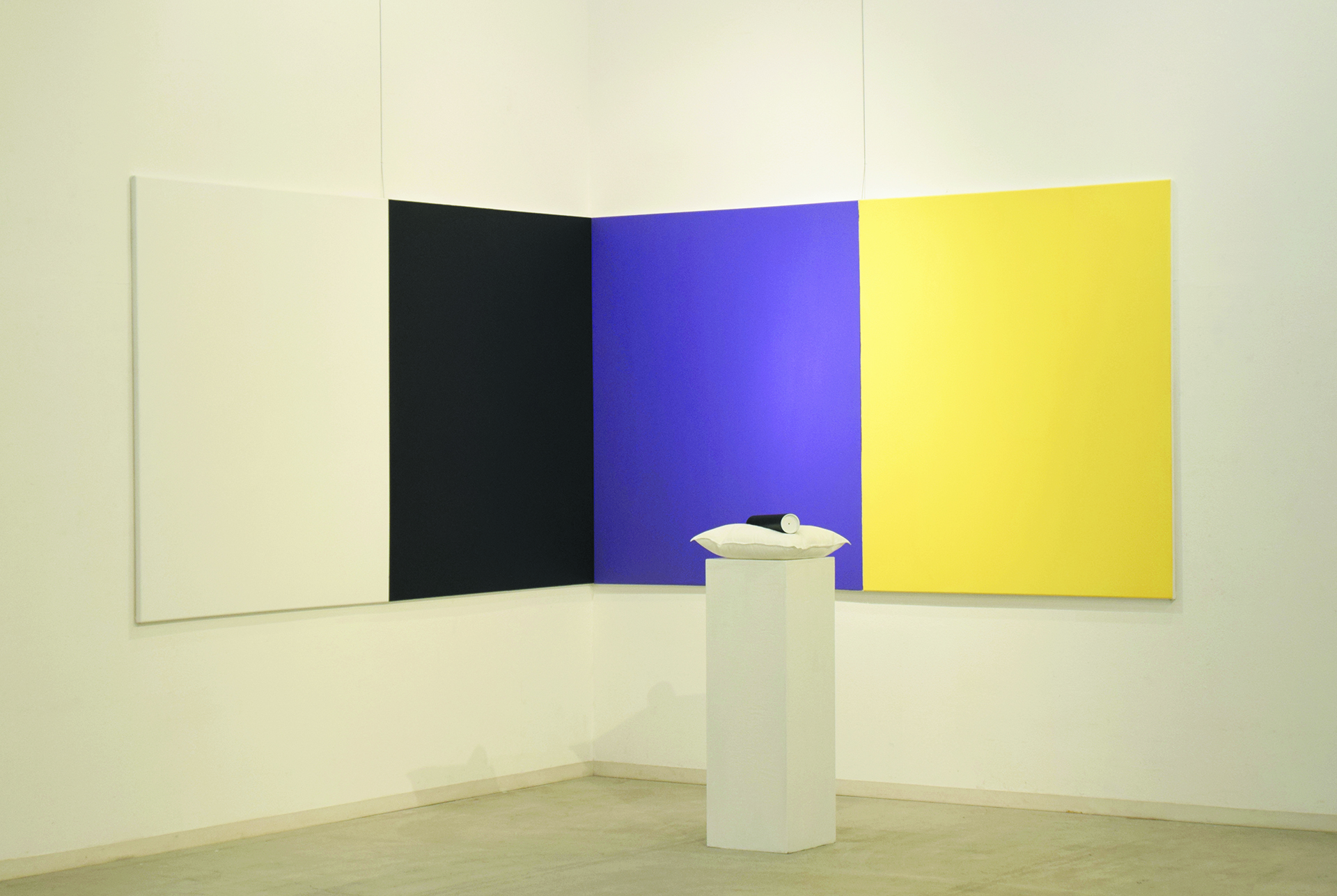 Wystawa; cztery płótna w różnych kolorach wiszące na ścianie w rogu, przed podest z tubą na poduszce.